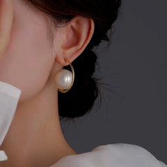 Close-up of large white pearl gold open hoop earring worn on ear, white top visible