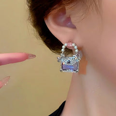 Side closeup of purple handbag style pearl stud earring worn on ear