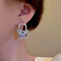 Front closeup of purple mini handbag pearl stud earring on ear