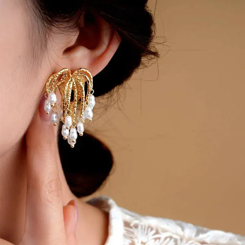 Gold firework design pearl drop statement earrings worn on woman's ear
