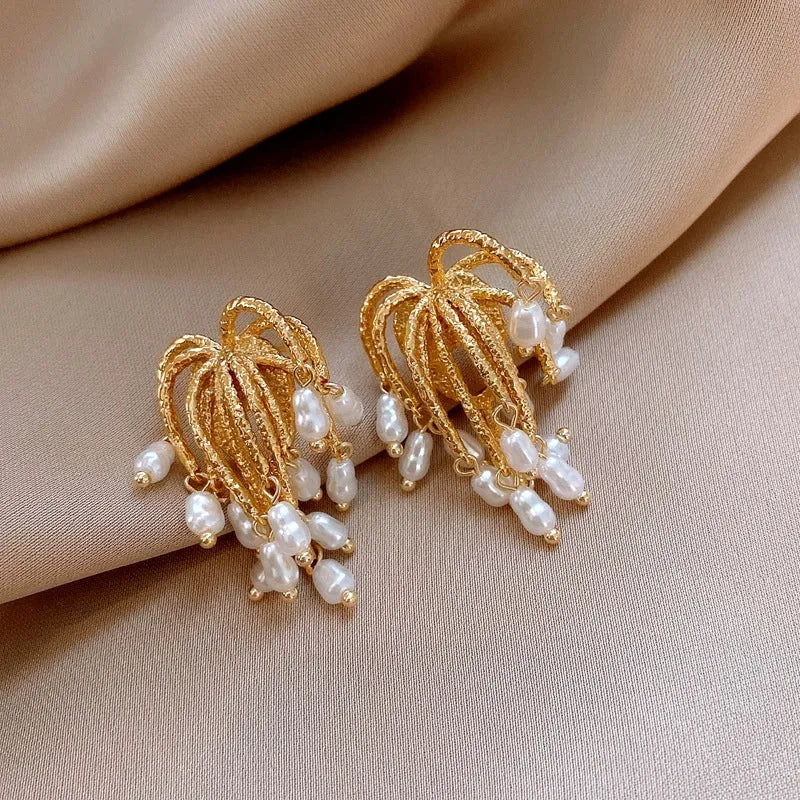 Pair of textured gold pearl drop chandelier earrings on beige satin fabric