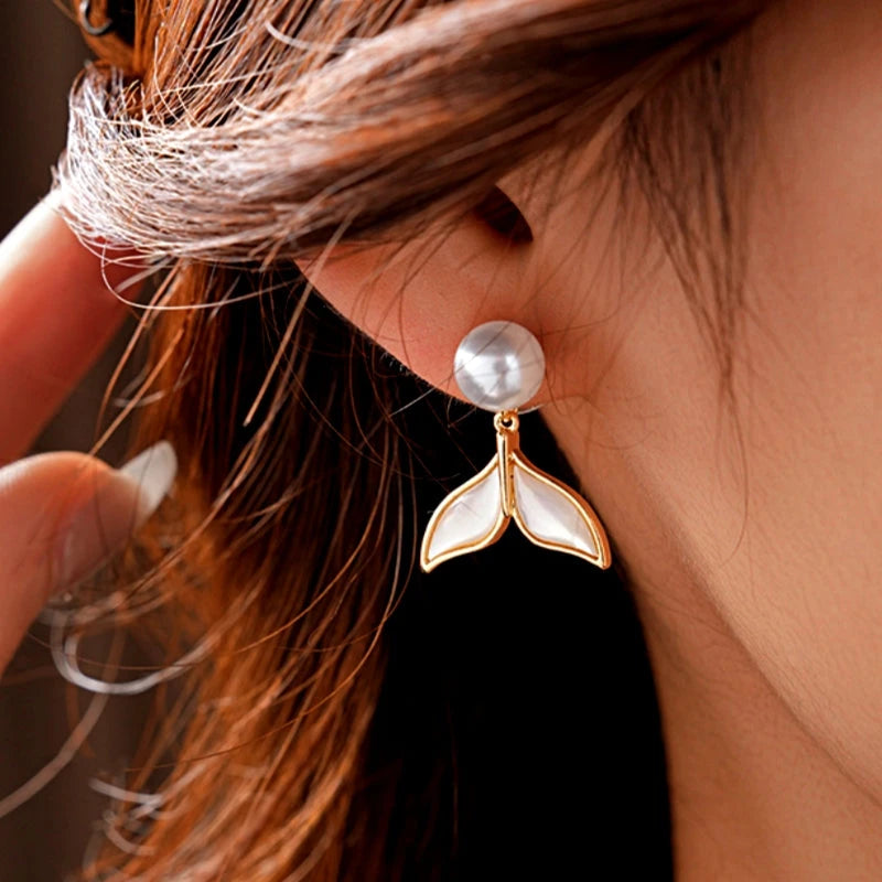 Close-up of gold pearl mermaid tail drop earring worn on a woman's ear