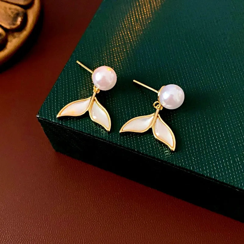 Pair of gold pearl mermaid tail drop earrings on dark green jewelry box