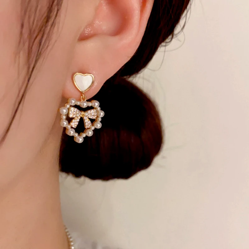 Model showcasing the dangle and style of the 14K Gold-Plated Pearl Heart Zircon Bow Earrings