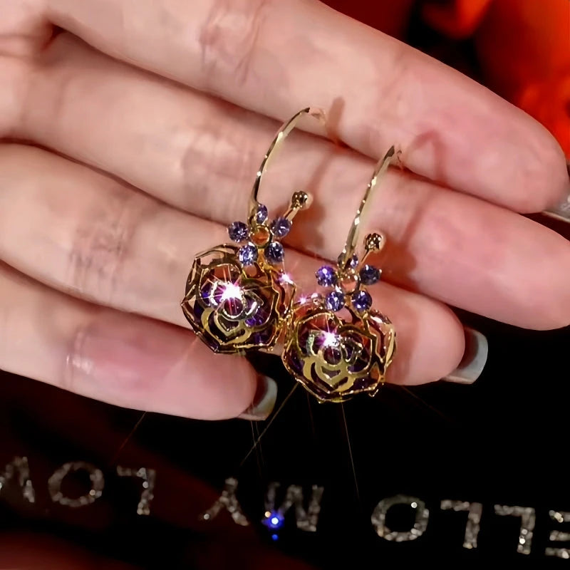 Gold hollow rose purple rhinestone hoop drop earrings held in hand