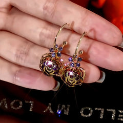 Gold hollow rose purple rhinestone hoop drop earrings held in hand
