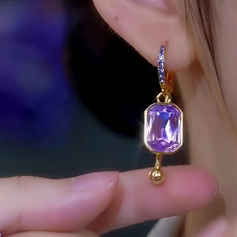 Purple emerald-cut crystal gold drop hoop earring worn on ear, closeup