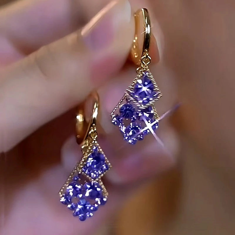 Pair of gold purple crystal double rhombus huggie drop earrings held in hand
