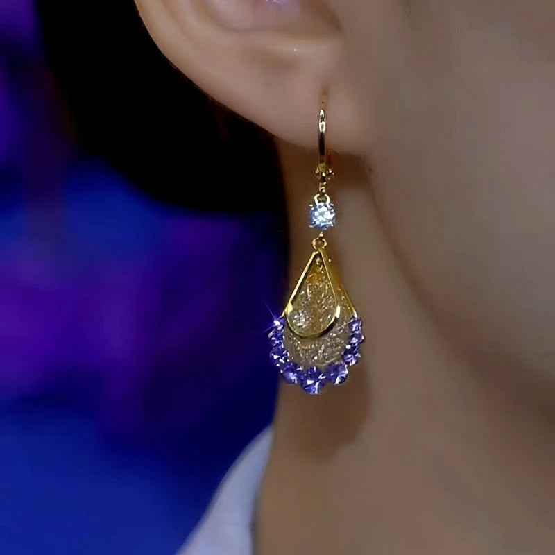 Purple crystal gold teardrop drop earring worn on woman's ear, side close-up