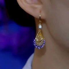 Purple crystal gold teardrop drop earring worn on woman's ear, side close-up
