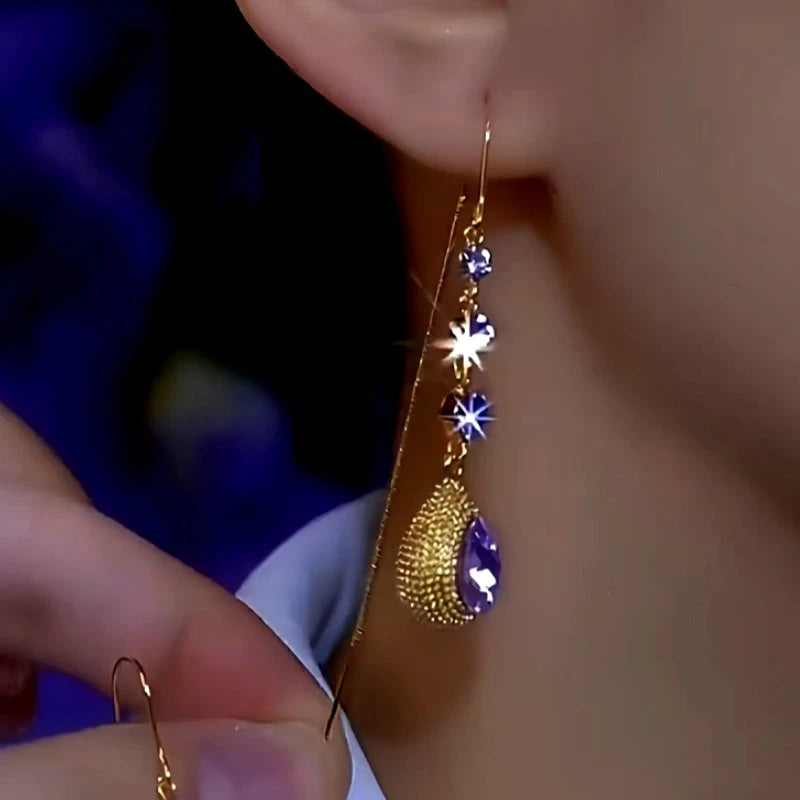 Gold purple crystal long dangle earring being worn on ear close-up
