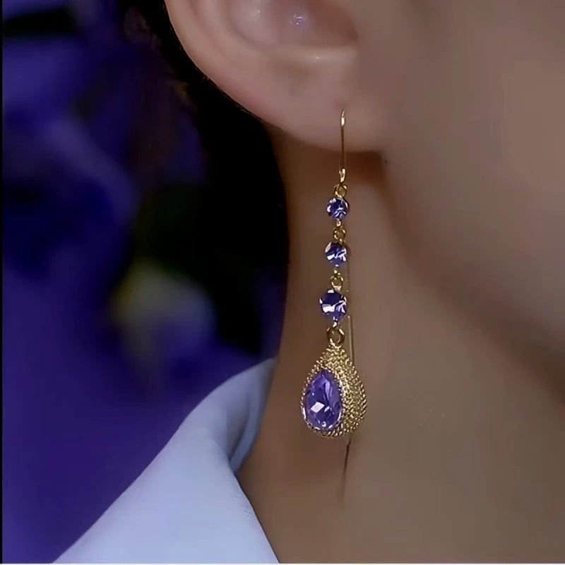Gold long dangle earring with purple teardrop crystals worn on woman's ear