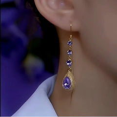 Gold long dangle earring with purple teardrop crystals worn on woman's ear