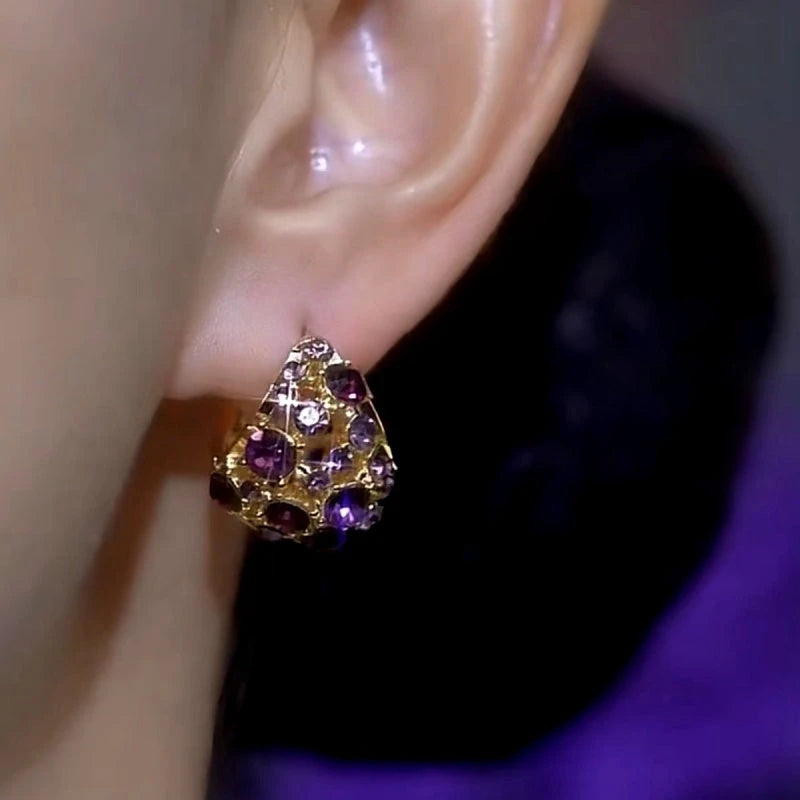 Gold purple rhinestone triangular stud earring worn on earlobe