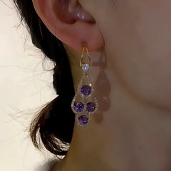Purple crystal gold drop dangle earring worn on woman's ear
