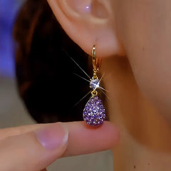 Sparkling purple teardrop gold dangle hoop earring on ear with finger below