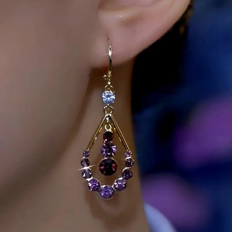 Closeup of gold purple crystal teardrop dangle earring worn on ear