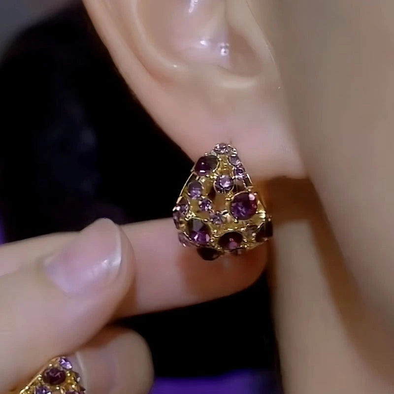 Purple rhinestone triangular stud earring held against earlobe