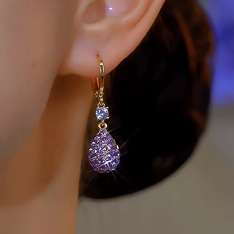 Gold purple teardrop crystal dangle hoop earring worn on female ear close-up