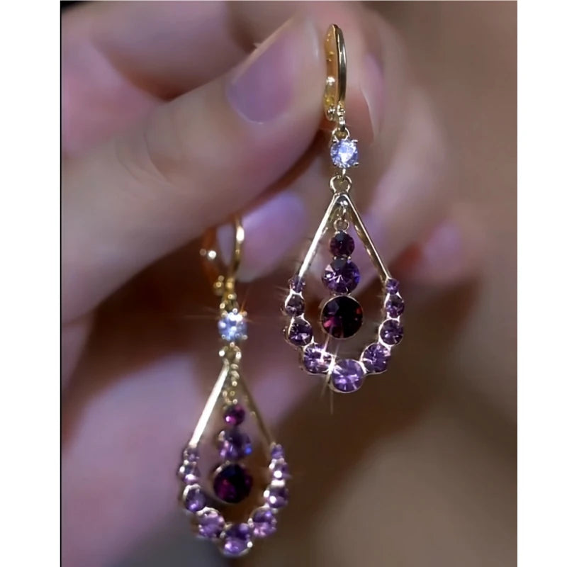 Pair of gold purple crystal teardrop dangle earrings held in hand