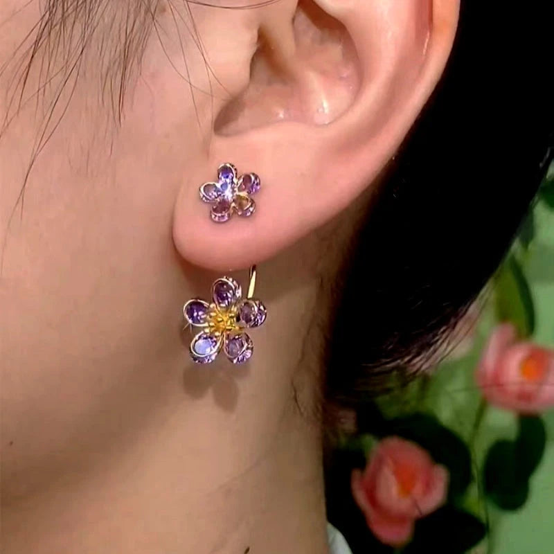 Purple flower gold hoop earring worn on a woman's earlobe