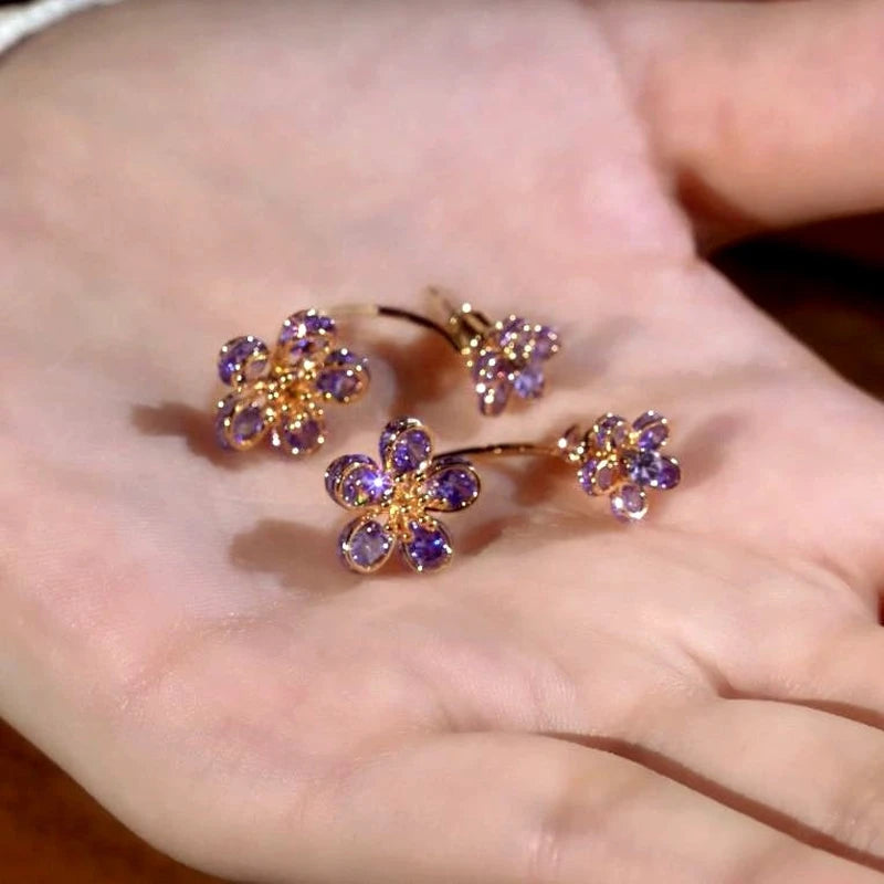 Pair of purple crystal flower gold hoop earrings resting on an open palm