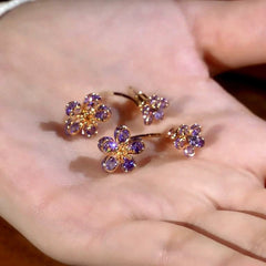 Pair of purple crystal flower gold hoop earrings resting on an open palm