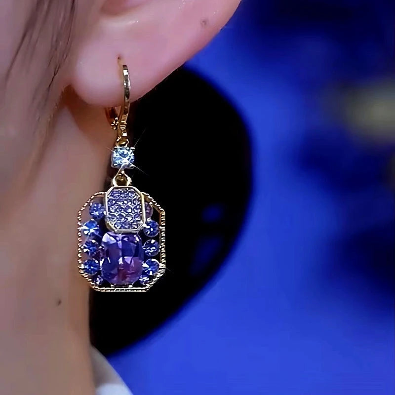 Purple blue crystal gold-tone drop earring worn on right ear