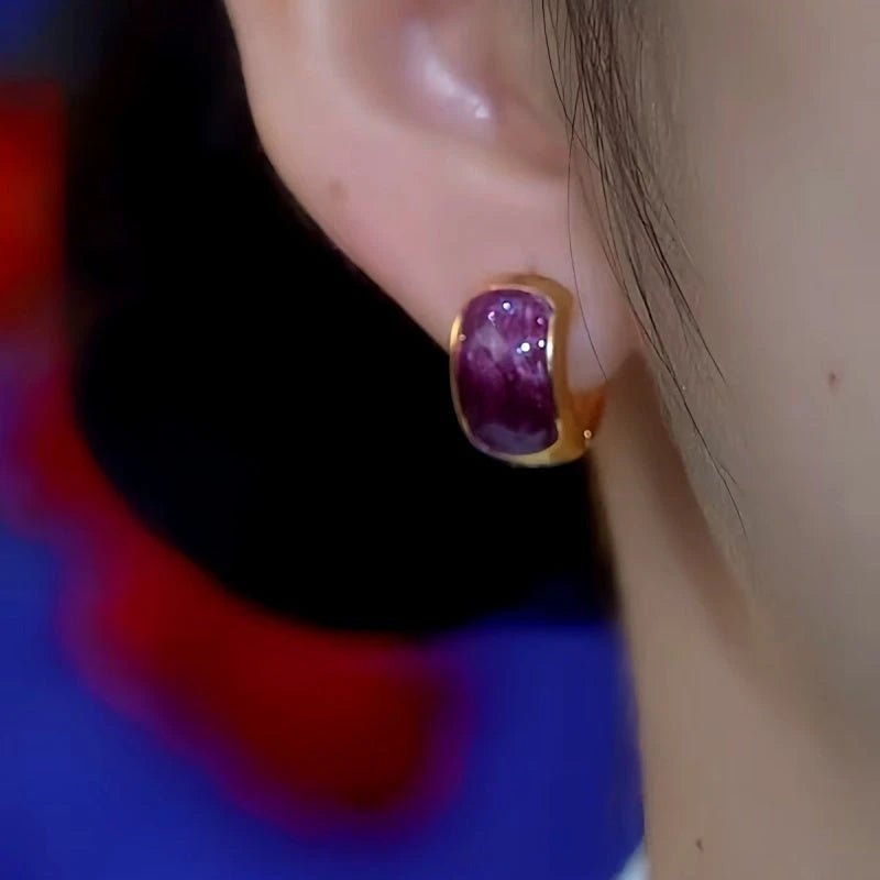 Purple gemstone gold huggie earring worn on a person's earlobe
