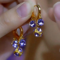 Pair of gold purple crystal dangle drop earrings held between fingertips
