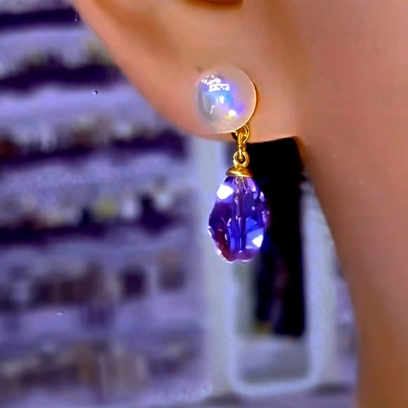 Gold tone iridescent pearl purple faceted teardrop crystal drop earring worn on ear (front view)