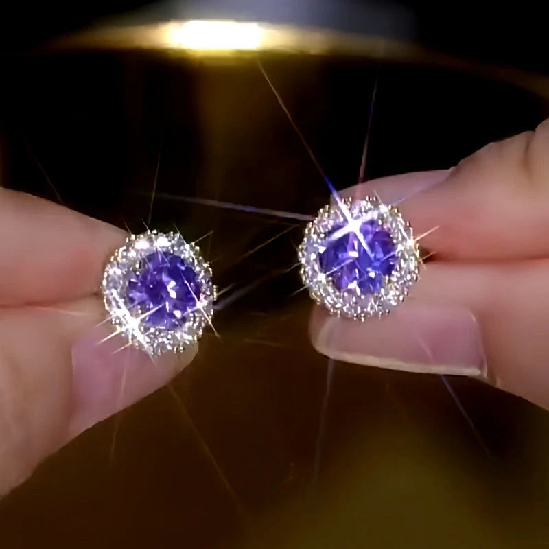Sparkling purple center stone halo stud earrings held between fingertips