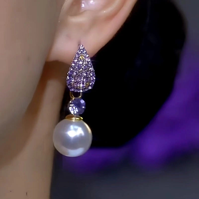 Purple rhinestone pearl drop earring worn on a person's ear