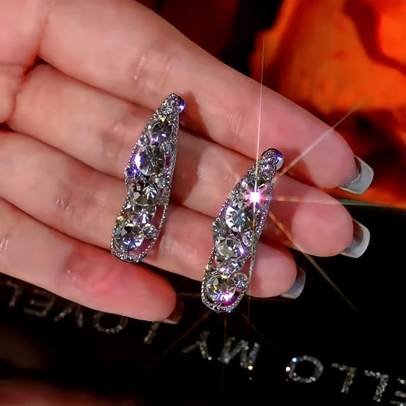 Pair of sparkly silver curved hoop statement earrings with pave crystal rhinestones held in hand