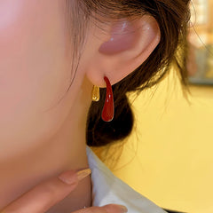 Close-up of red and gold front-back teardrop earrings worn on a woman's ear