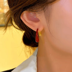 Alternate angle of red and gold front-back teardrop earrings worn on ear