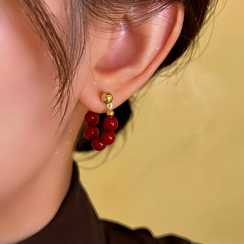 Side angle close-up of red beaded gold stud C-shaped hoop earring on woman's ear