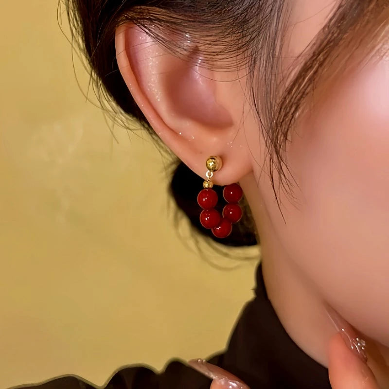 Close-up front view of red beaded gold stud C-shaped hoop earring on woman's ear
