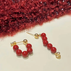 Pair of gold-tone red beaded half-hoop stud earrings on cream surface with red knit backdrop