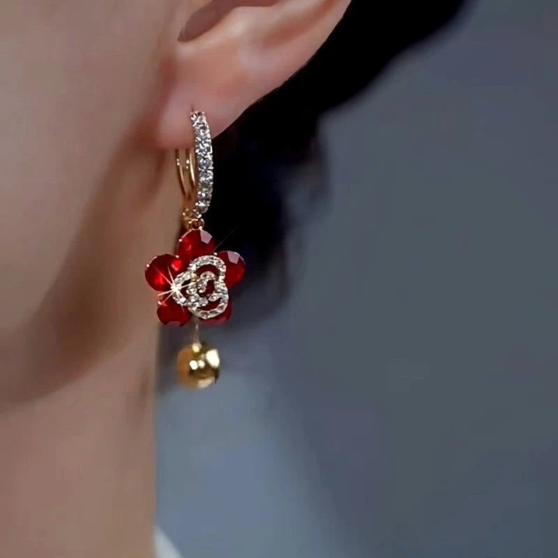 Close-up of red crystal flower gold ball drop hoop earring worn on ear