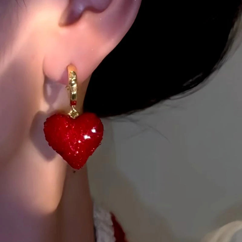 Close-up of glittery red heart gold drop earring worn on a woman's ear