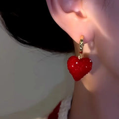Side view close-up of sparkly red heart gold hoop drop earring on ear