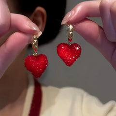 Pair of sparkly red heart gold hoop dangle earrings held in hands