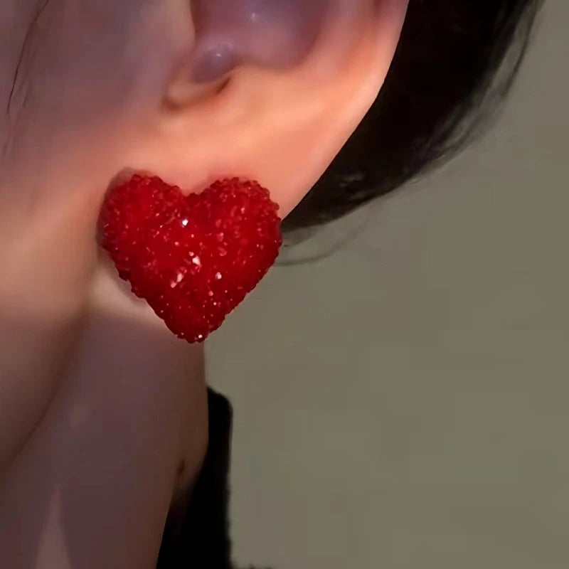 Side angle close-up of red sparkly heart stud earring on ear