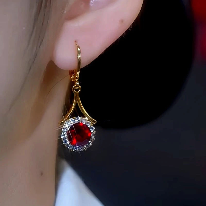 Gold ruby red gem drop earring with crystal halo worn on a woman's ear