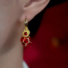 Women's gold red gem drop hoop earring worn on ear, side view