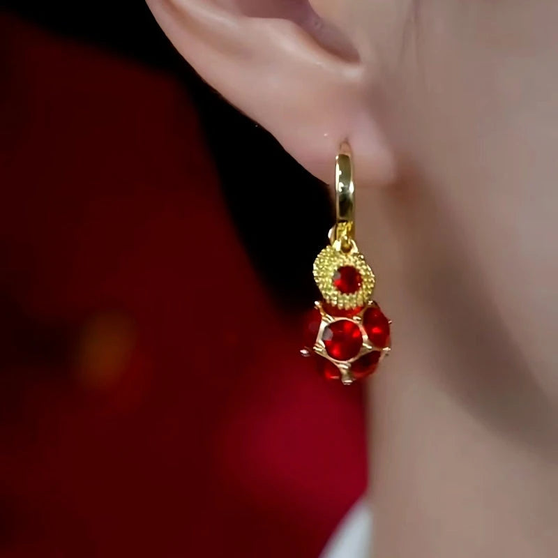 Women's red crystal gold dangle hoop earring worn on ear, front view