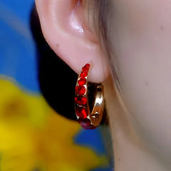 Gold red rhinestone huggie hoop earring worn on earlobe, side close-up