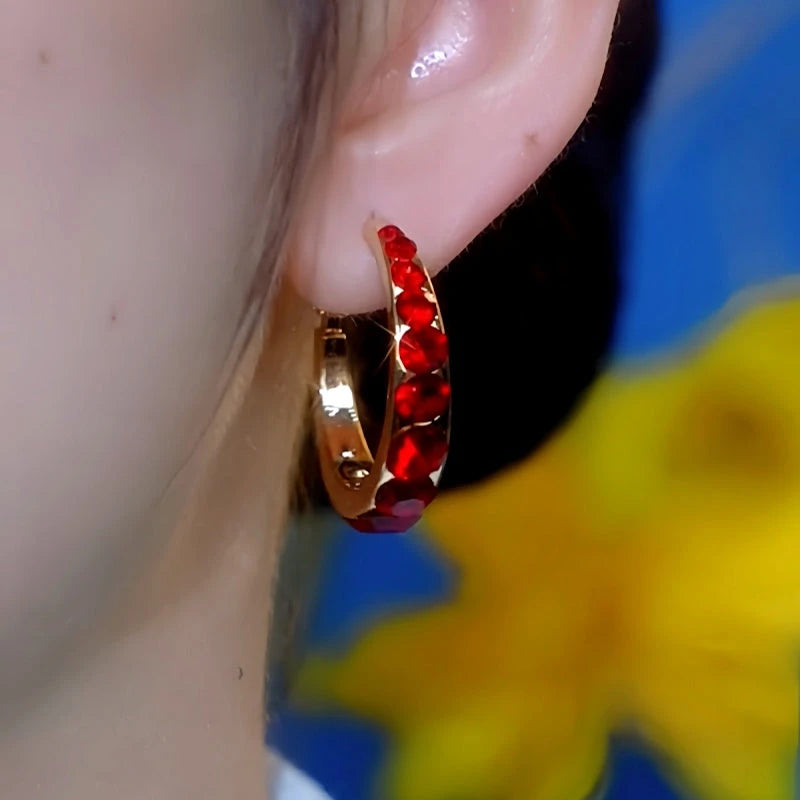 Red rhinestone gold huggie hoop earring on ear, front close-up view