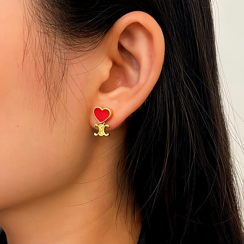 Model showcasing the dangle and style of the 14K Gold-Plated Red Heart Arc De Triomphe Earrings
